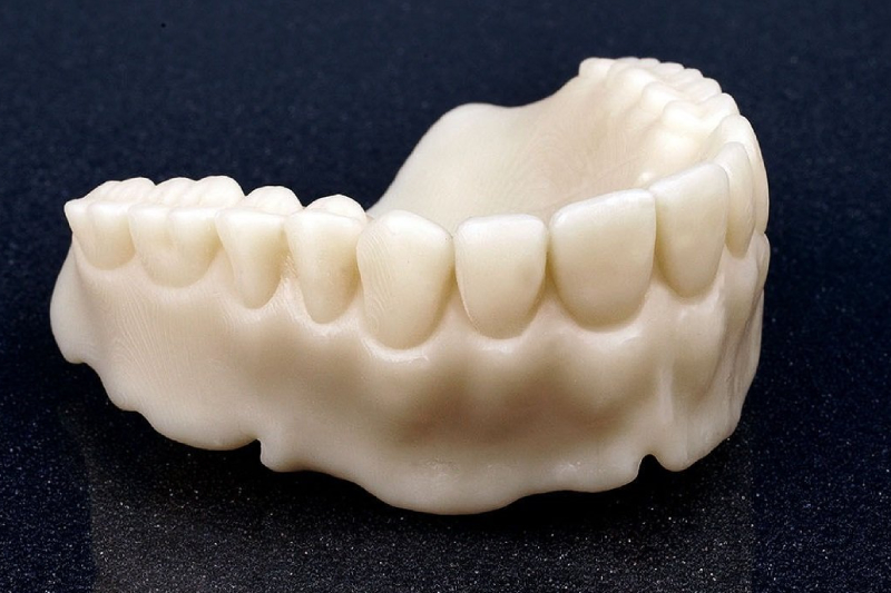 A closeup of 3D printed white teeth prototype on a black tile.