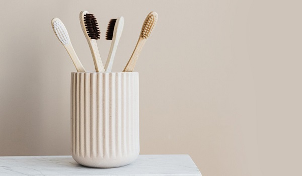 A white porcelain brush holder holds four bamboo toothbrushes with black, brown, and white bristles