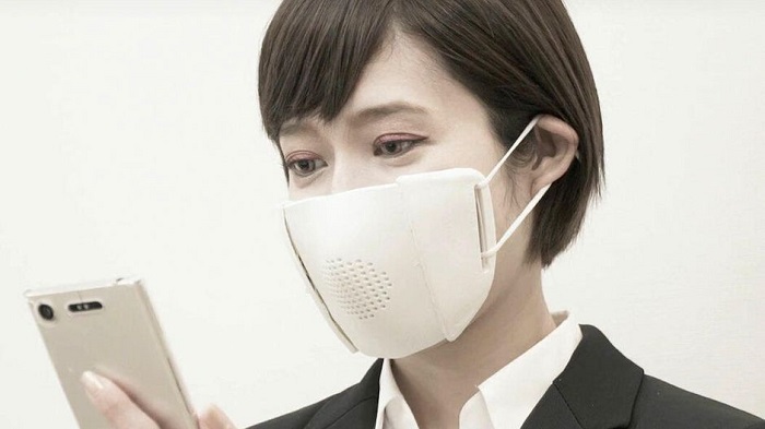 A lady has worn a mask on her mouth and looking at the smartphone that she has held in her hand.